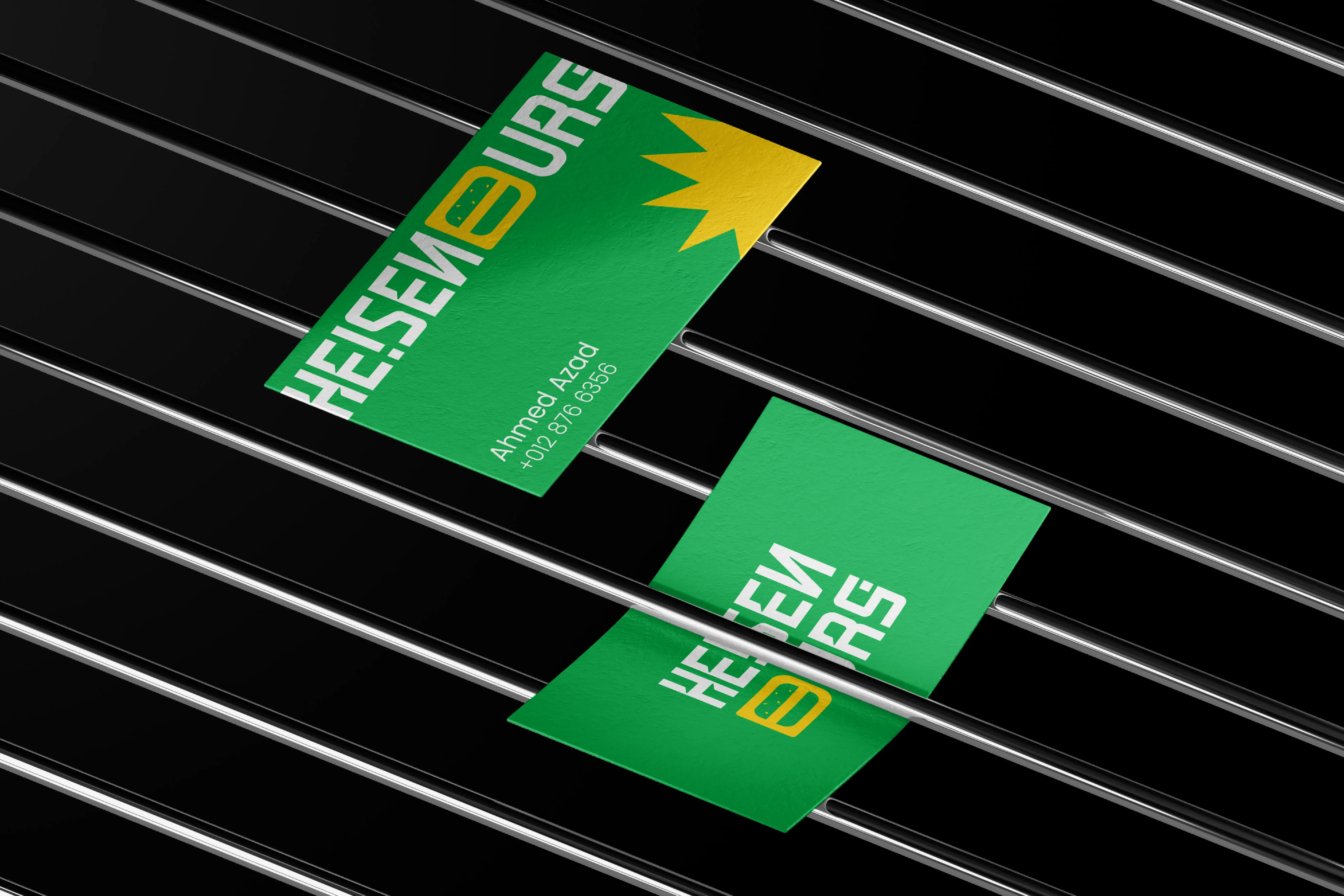 Heisenburg green business cards arranged across black metal bars, showing the geometric wordmark and yellow starburst.