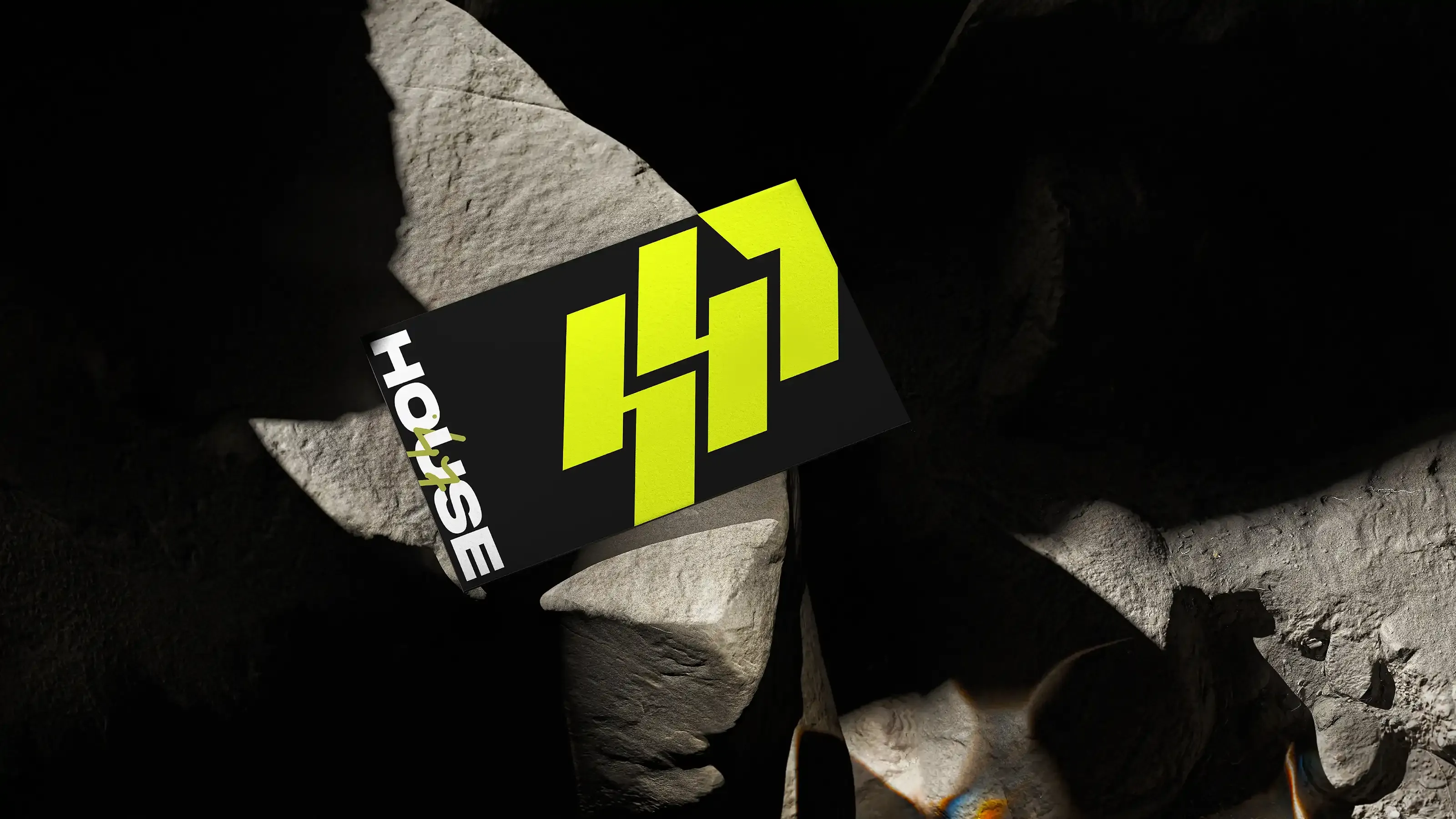 Electric-yellow House47 badge printed on a black card among dark rocks.