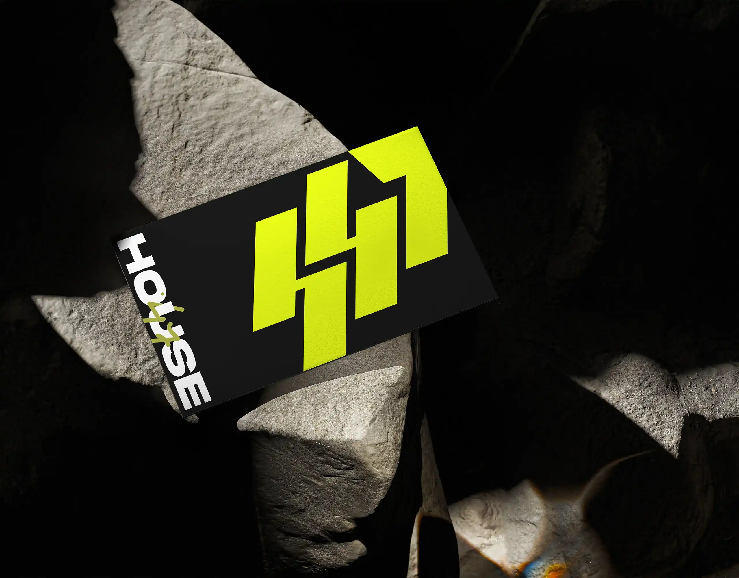 Electric-yellow House47 interlocking badge on a black card among dark rocks.